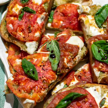 Pesto Caprese Garlic Bread drizzled with olive oil and balsamic vinegar on a serving platter.