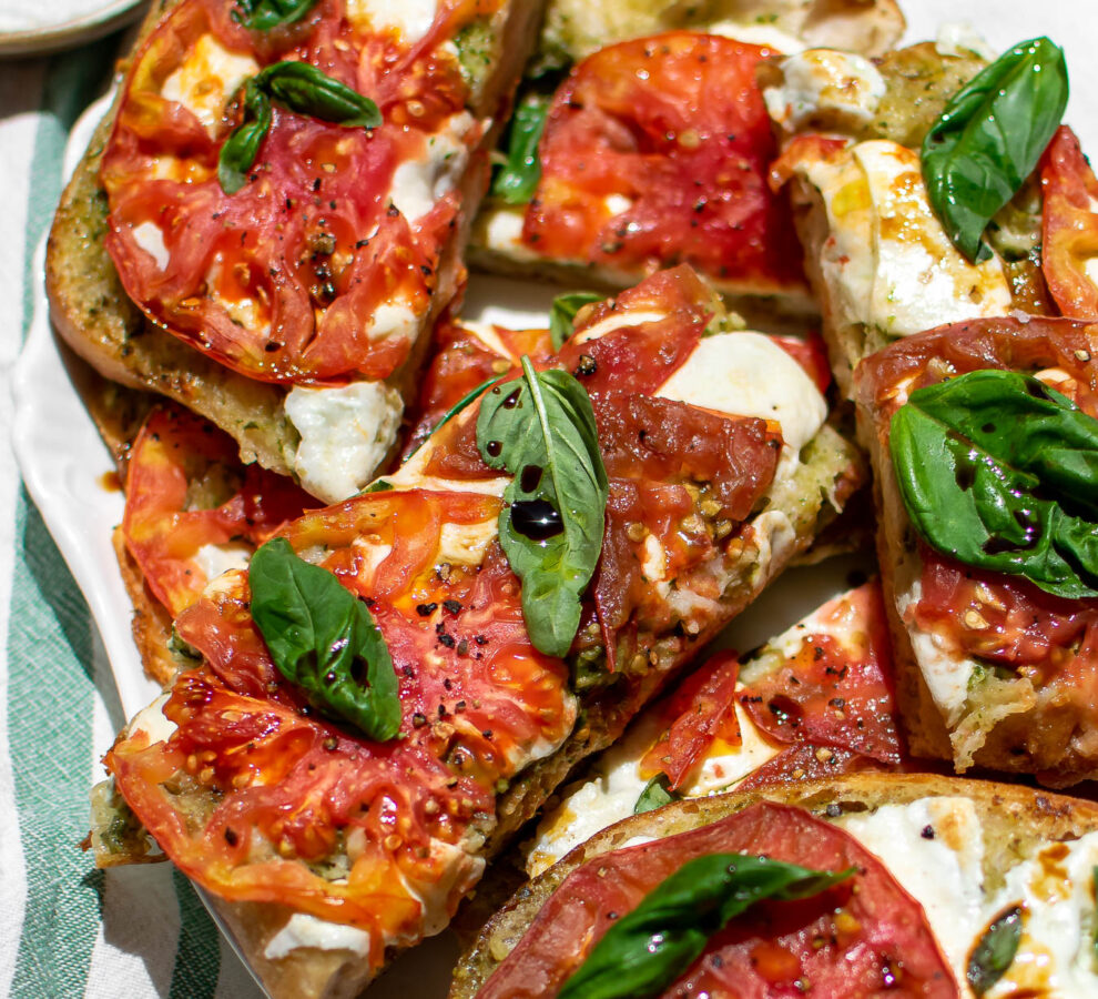 Pesto Caprese Garlic Bread drizzled with olive oil and balsamic vinegar on a serving platter.