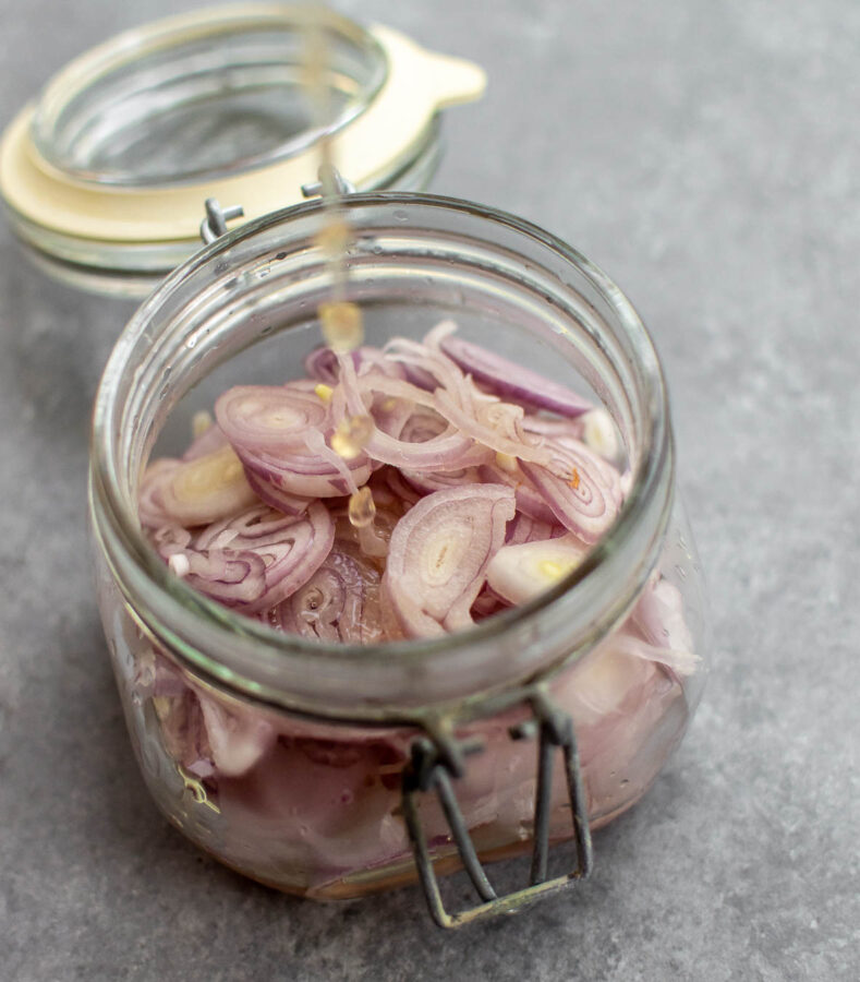 Pickling liquid being poured over the sliced shallots.