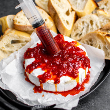 Pepper Jelly "blood" being injected into the baked brie with a syringe.