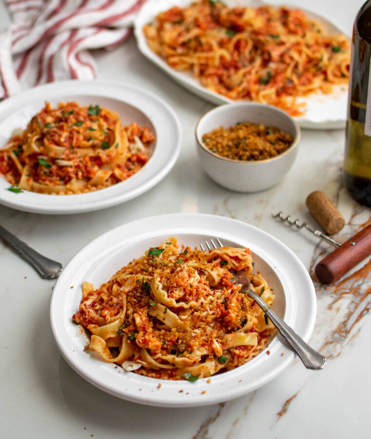 Photo of a table with a serving platter of pasta, two bowls of pasta, and a small bowl of fried breadcrumbs.